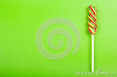 Bright juicy colored lollipop on a green paper background. Lollipop in the form of a color spiral. Fruit candy. Stock Photo