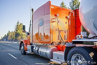 Bright orange big rig semi truck transporting tank semi trailer for transportation of liquid and liquefied chemical cargo running Stock Photo