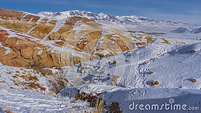 Bright orange hills and snow-capped mountains against the blue sky Stock Photo