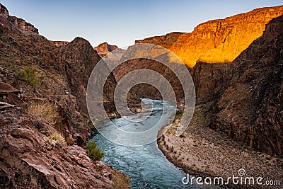 Bright Orange Light Warms The Rocks Above The Colorado River At Sunrise Stock Photo