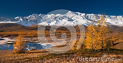 Bright picturesque autumn landscape with mountains covered with snow, forest, yellow larches and beautiful lake with reflections Stock Photo
