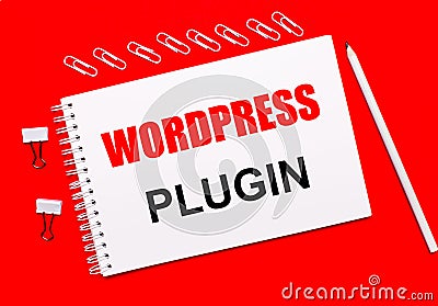 On a bright red background, a white pencil, white paper clips, and a white notebook with the text WORDPRESS PLUGIN Stock Photo