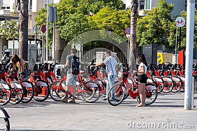 Bright red bicycles available for rent parked in a row at La Barceloneta. Concept of environmentally sustainable transport. Bike Editorial Stock Photo