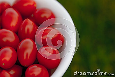 Bright red cherry tomatoes in a white bowl on a green lawn. Stock Photo