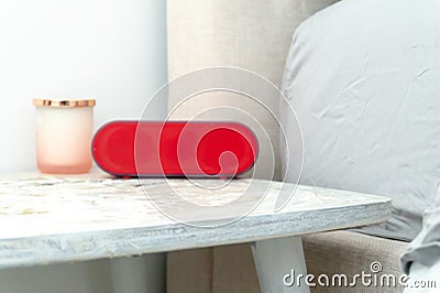 Bright red alarm clock and candle jar on a bedside table nightstand, with bed and linens showing in soft colors Stock Photo