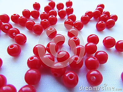 Bright red round beads for needlework are randomly scattered over a white background Stock Photo