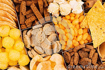 Bright spicy snacks collection - popcorn, nachos, potatoes chips, croutons, corn sticks as chess background. Stock Photo