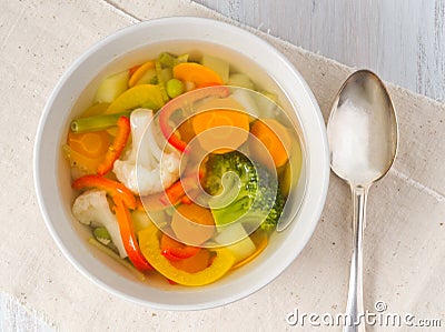 Bright spring vegetable soup with cauliflower, broccoli, pepper, carrot, green peas. Top view, white wooden background. Stock Photo