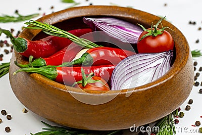 Bright summer vegetables: onion, garlic, tomato, red chili pepper, rosemary in brown wooden bowl and peppercorns on white table Stock Photo