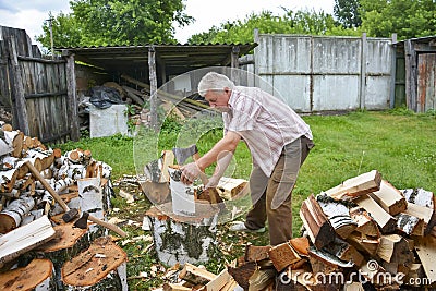 On a sunny summer day, a man is chopping firewood in the yard Stock Photo