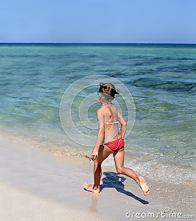 A sunny photo of a little girl in bikini running along a sea shore Stock Photo