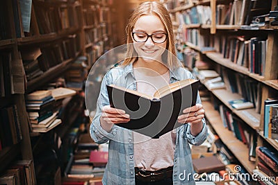 Bright and warm picture of clever student reading a book. Girl is smiling and continue to read book further. Stock Photo