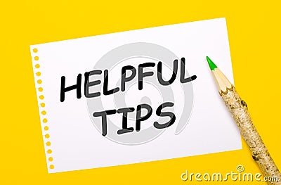 On a bright yellow background, a large wooden pencil and a white sheet of paper with the text HELPFUL TIPS Stock Photo