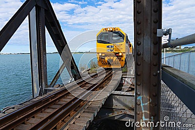 Bright yellow diesel train entering truss bridge Editorial Stock Photo