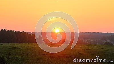 Bright yellow disk of the sun sits at the horizon of the forest and the towers of power lines against orange sunset. Stock Photo