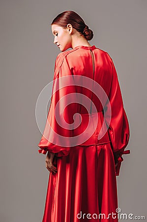 Bright young lady in red dress with long wide sleeves and sexy neckline on high heels mooving on grey studio background Stock Photo