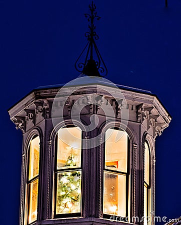 Brightly lit Christmas tree beams brightly from a cupola atop a white New Eland style house Stock Photo