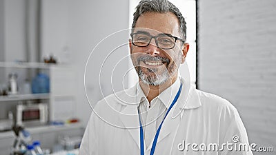 Brimming with confidence, smiling young hispanic man, grey-haired scientist standing in the lab amidst experiments Stock Photo