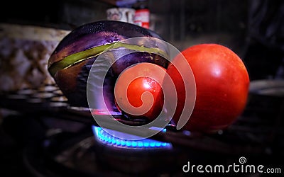 Brinjal or eggplant and tomatoes are being roasted on the fire flame of the gas stove. Stock Photo