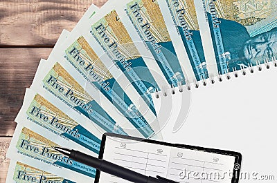 5 British pounds bills fan and notepad with contact book and black pen. Concept of financial planning and business strategy Editorial Stock Photo