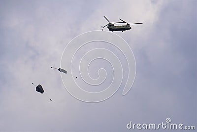 Paratrooper descends with open grey parachute from Chinook Stock Photo