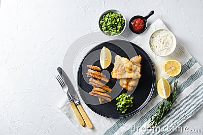 British Traditional Fish and chips with minty mashed peas detail and a slice of lemon. on black round plate over white lintn and Stock Photo