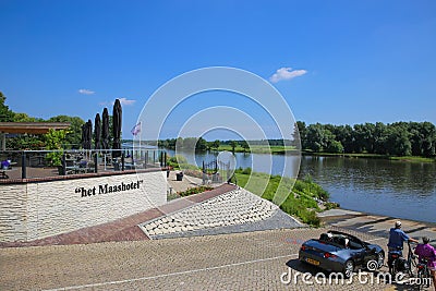 View beyond hotel terrace with outdoor restaurant on people waiting for ferry to arcen over river maas in summer Editorial Stock Photo