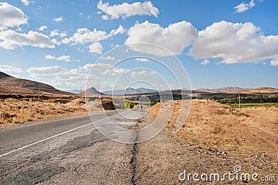 Broken asphalt road in the dry grass valley of the Middle East under white clouds Stock Photo