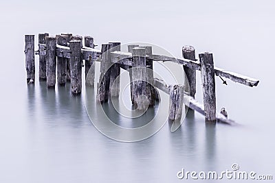 Broken down old pier posts in calm water, covered with light dusting of snow Stock Photo