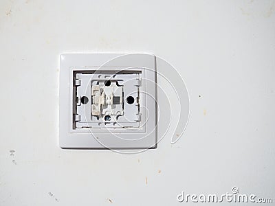 Broken electrical switch on the wall. Switch without button. Disassembled device. White wall with electric light switch. Stock Photo