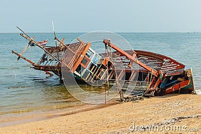 A broken fishing ship lies on its side near the shore, shipwrecked Stock Photo