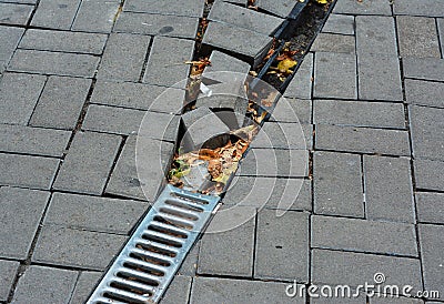 Broken rain gutter downspout pipe for roof runoff with damaged open water drainage in the pavement to repair. Stock Photo