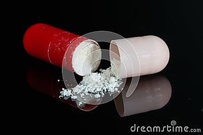 Broken red and pink antibiotic capsule on black Stock Photo