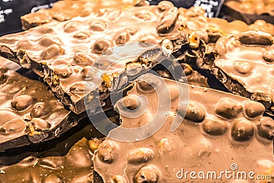 The broken tile of milk chocolate with whole nuts in supermarket. Texture or background. Sweets. Natural product. Useful elements. Stock Photo