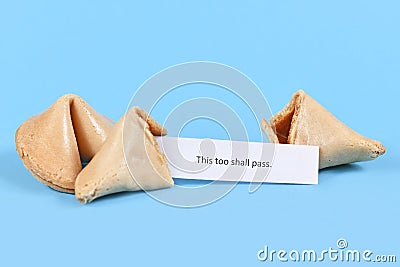 Broken up and whole fortune cookie with motivational text `This too shall pass` on paper note on blue background Stock Photo