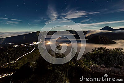 Bromo volcano crater erupt release smoke at the night with village car light tail star sky background landscape at Indonesia Bromo Stock Photo