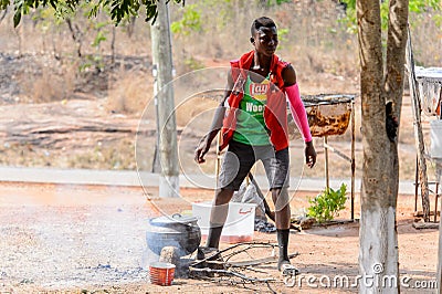 Unidentified Ghanaian man in colored clothes cooks on fire. Editorial Stock Photo