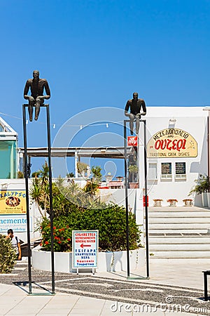 Bronze sculptures of two men sitting on horizontal bars near the Orthodox Metropolitan Cathedral of Ypapanti in Fira village Editorial Stock Photo