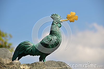 The bronze statue of a cock with golden cloverleaf in its beak. Editorial Stock Photo