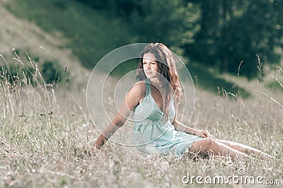 Brooding young woman sitting on the grass of a summer meadow. Stock Photo