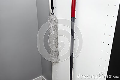 Broom and duster hanging in a built-in kitchen cupboard, black pantry door open. Stock Photo