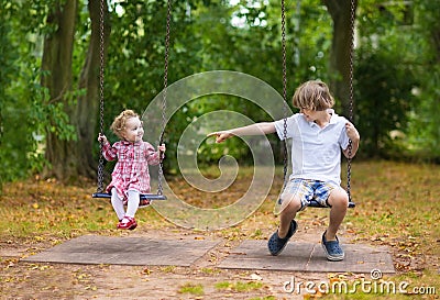 Brother and baby sister on swing on playground Stock Photo