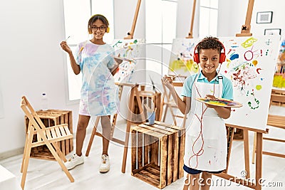 Brother and sister listening to music holding paintbrush and palette at art studio Stock Photo