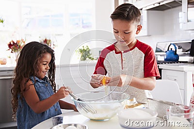 Brother and sister preparing cake mixture together at the kitchen table, waist up Stock Photo