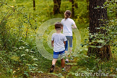 Brother and sister in white t-shirts go into the woods on the path in the summer Stock Photo