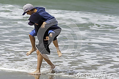 Brothers playing piggyback at the edge of waves on coast Stock Photo