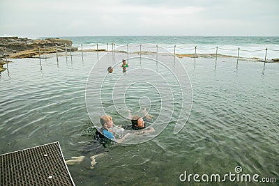 Brothers swimming at the Bogey Hole in Newcastle, NSW on an overcast day with rough surf Stock Photo