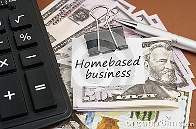On a brown background lies a calculator and dollars on a clip with an inscription on paper - Homebased business Stock Photo