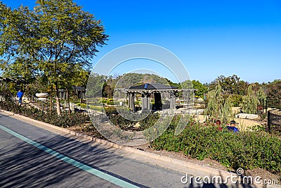 A brown and black pergola in the garden surrounded by a dirt path and lush green trees and plants Editorial Stock Photo