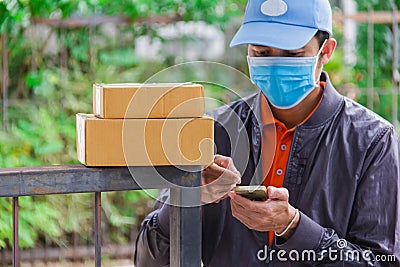 Brown cardboard box put on metal fence with delivery man wear hygienic mask and blue cap on background Stock Photo